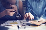 Two people holding a tablet and a pen, brainstorming over papers