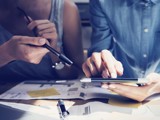 Two people holding a tablet and a pen, brainstorming over papers