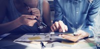 Two people holding a tablet and a pen, brainstorming over papers