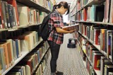 Student standing and reading book in the library aisle