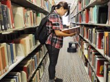 Student standing and reading book in the library aisle