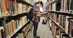 Student standing and reading book in the library aisle